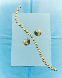 Gold chain bracelet and matching earrings arranged on a light blue paper backdrop for D Repubblica