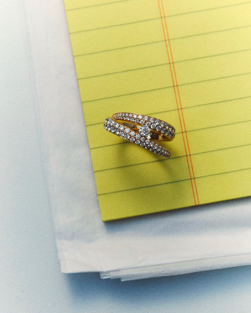 Close-up of a diamond and gold crossover ring resting on a yellow lined notepad for D Repubblica Paper Love editorial.