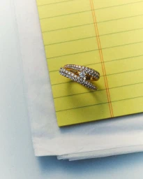 Close-up of a diamond and gold crossover ring resting on a yellow lined notepad for D Repubblica Paper Love editorial.