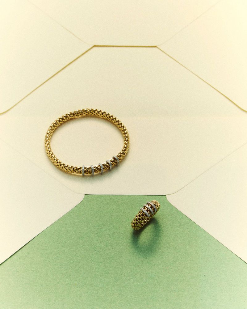 Gold mesh bracelet and ring resting on geometric paper shapes in cream and green