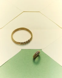 Gold mesh bracelet and ring resting on geometric paper shapes in cream and green