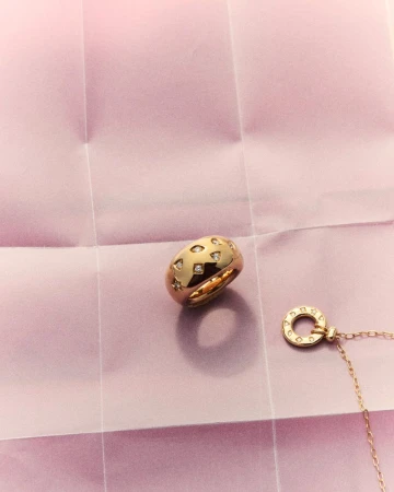 Gold ring with diamond accents and matching necklace resting on a creased pink paper background