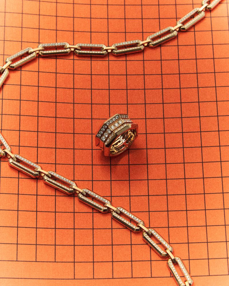 Gold chain necklace with diamonds and matching ring resting on orange grid paper