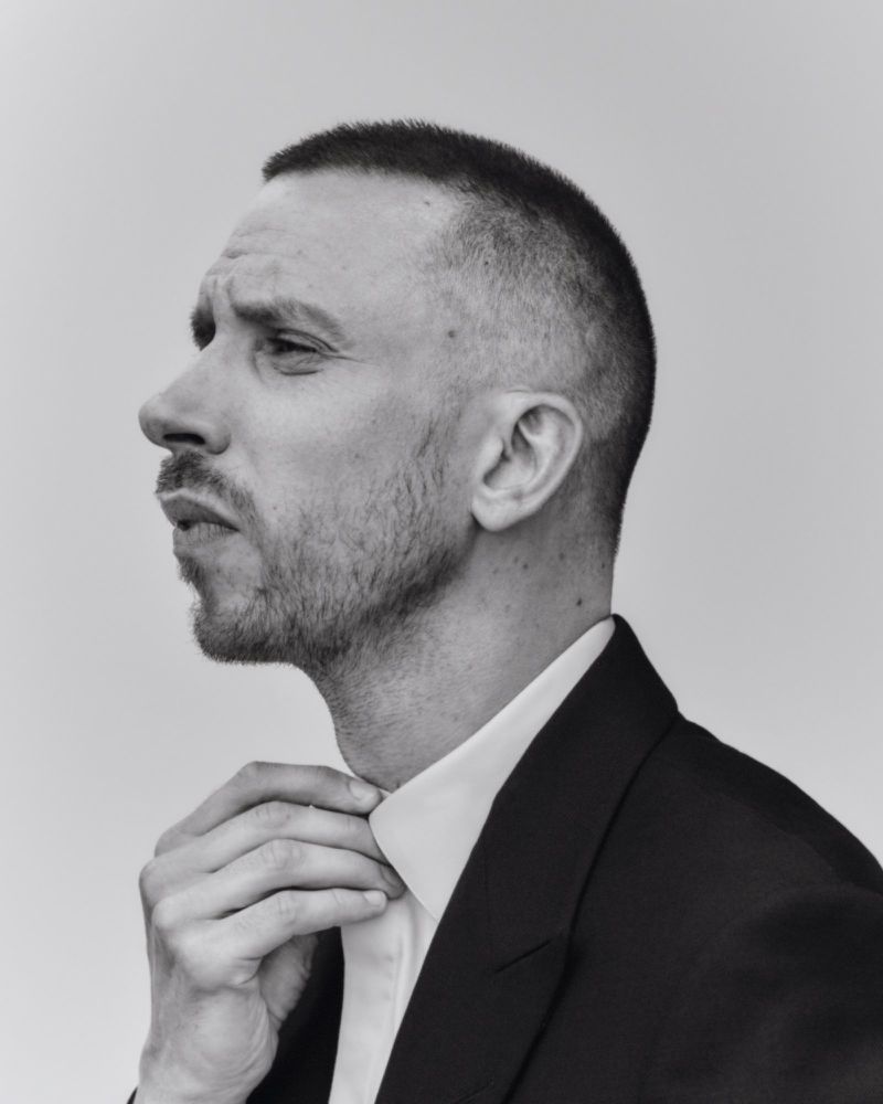 Monochrome profile portrait of a man adjusting his shirt collar while wearing a dark jacket