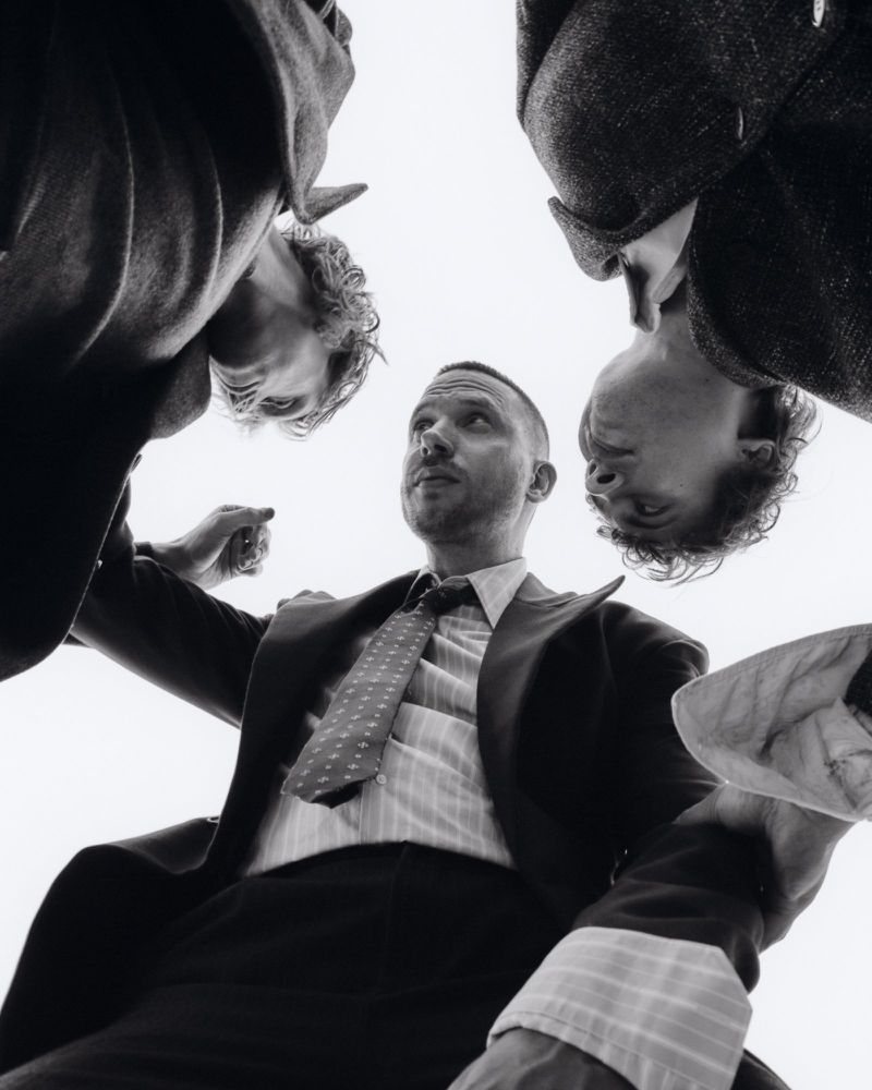Low angle monochrome shot of three men looking down in tailoring against a bright sky.