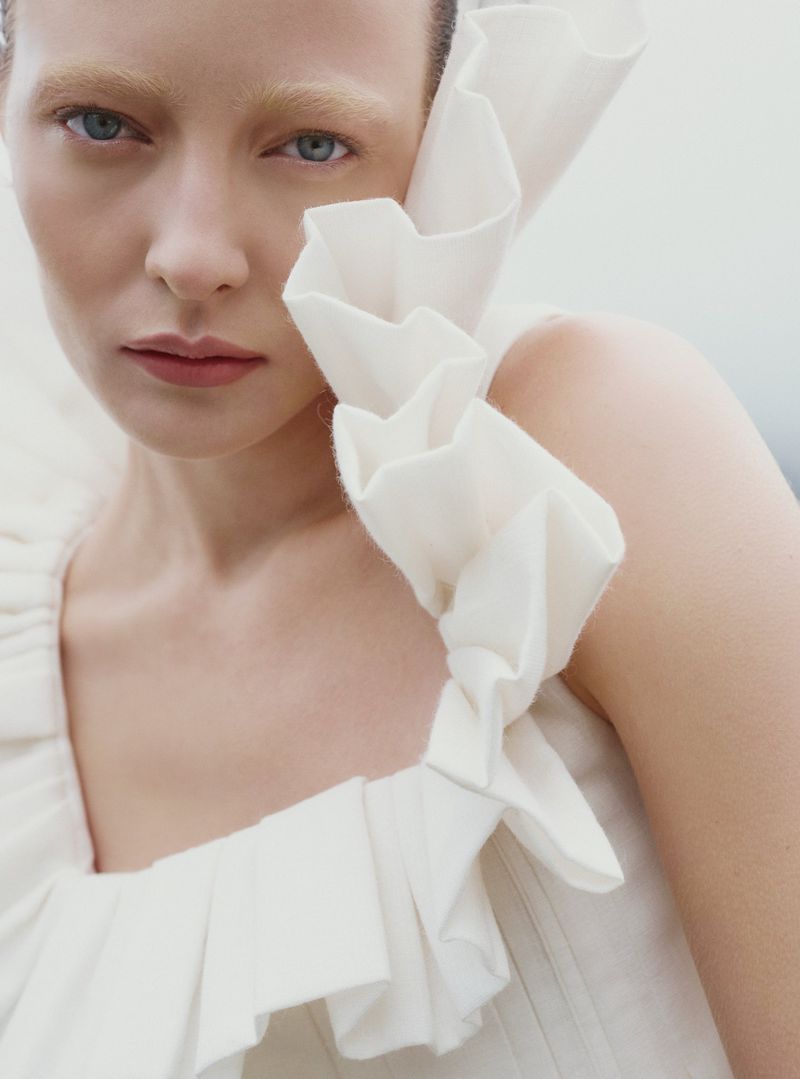 Close-up portrait of a woman wearing a white ruffled top against an overcast sky background.