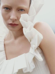 Close-up portrait of a woman wearing a white ruffled top against an overcast sky background.