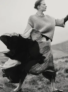 Model in a knit sweater and voluminous pleated skirt outdoors in a landscape photographed by Agata Pospieszynska for Harper's Bazaar UK