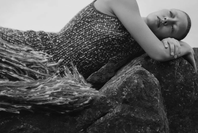 Model lying on dark rocky terrain wearing a textured patterned sleeveless knit dress