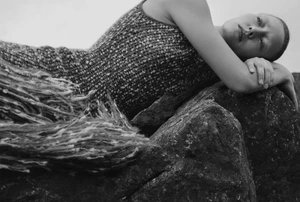 Model lying on dark rocky terrain wearing a textured patterned sleeveless knit dress