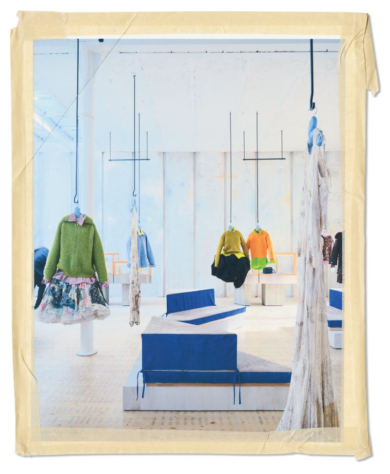 Interior of an American Vogue fashion editorial space featuring garments suspended from ceiling hooks and blue and white seating platforms.