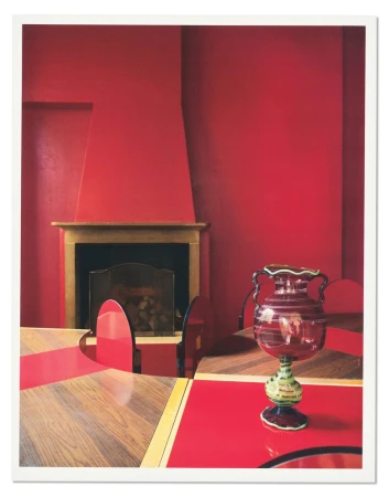Decorative red and green glass vase on a red tabletop inside a room with vibrant red walls and a fireplace