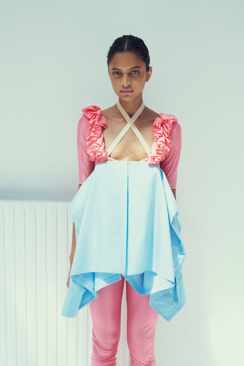 Model wearing a pink top with ruffled straps and light blue layered tunic against a white wall