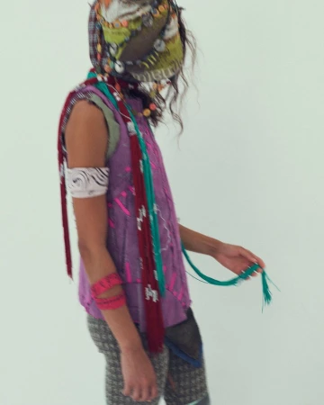 Model in layered purple sleeveless top and patterned leggings wearing a decorated headscarf against a white background.