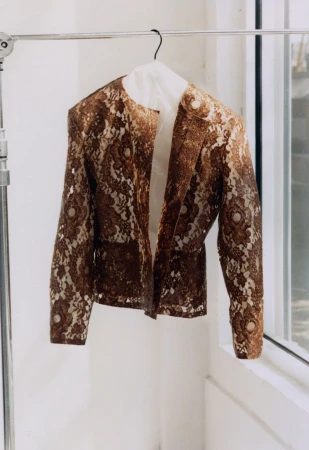 Brown lace jacket hanging on a garment rack against a bright white studio window background