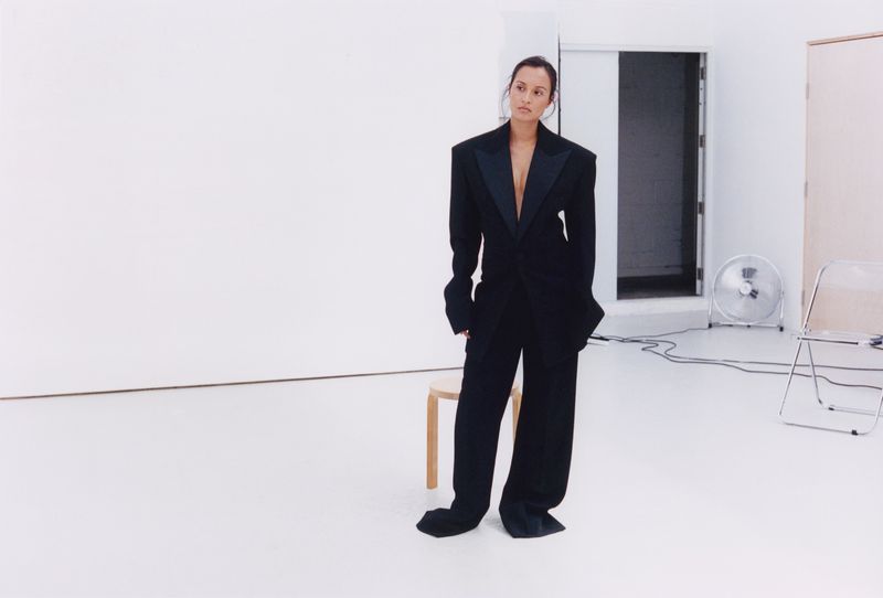 Woman in an oversized black tuxedo suit standing in a white studio setting for Pop Magazine editorial.