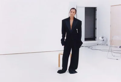 Woman in an oversized black tuxedo suit standing in a white studio setting for Pop Magazine editorial.