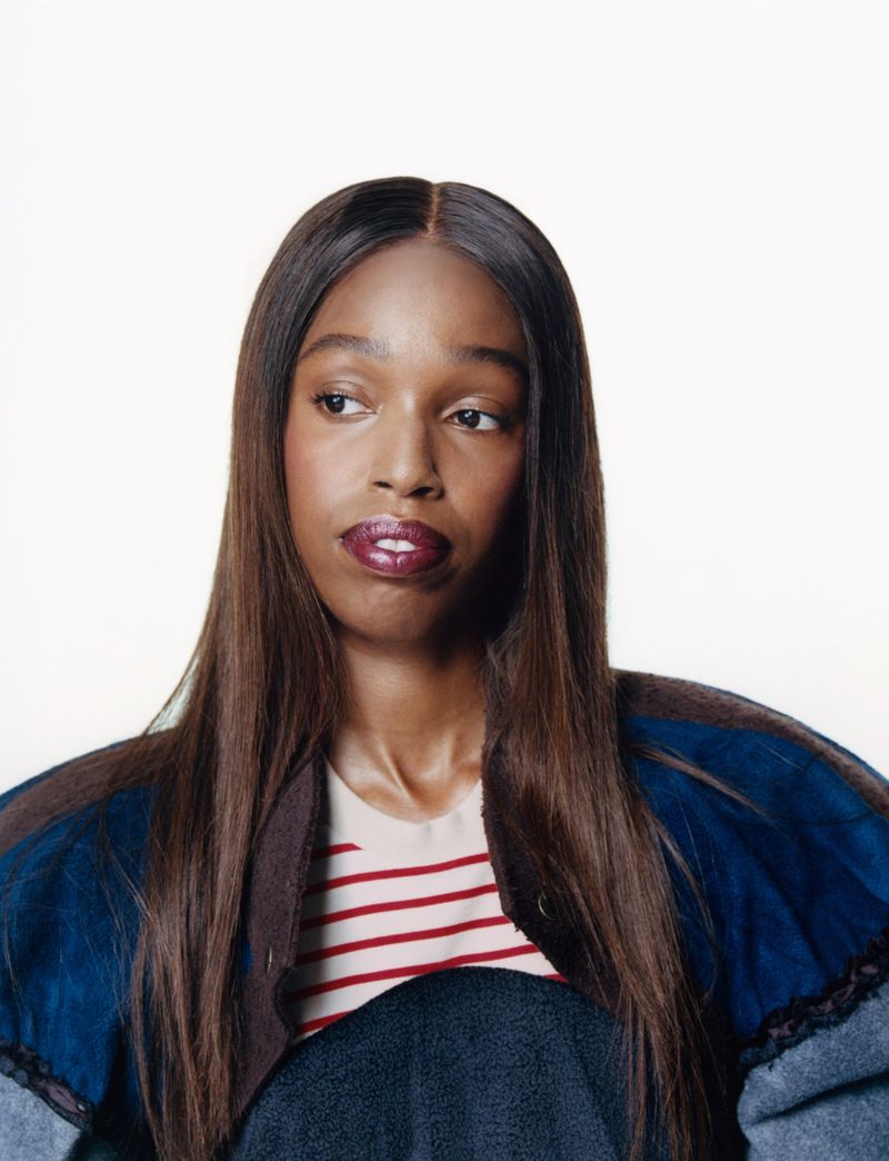 Portrait of a woman with long dark hair wearing a striped top and layered jacket against a plain white background.