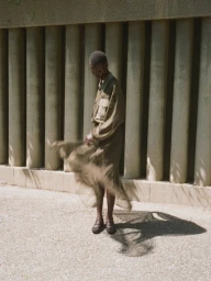 A model standing in front of concrete pillars wearing a utility shirt and sheer skirt, captured with motion blur.