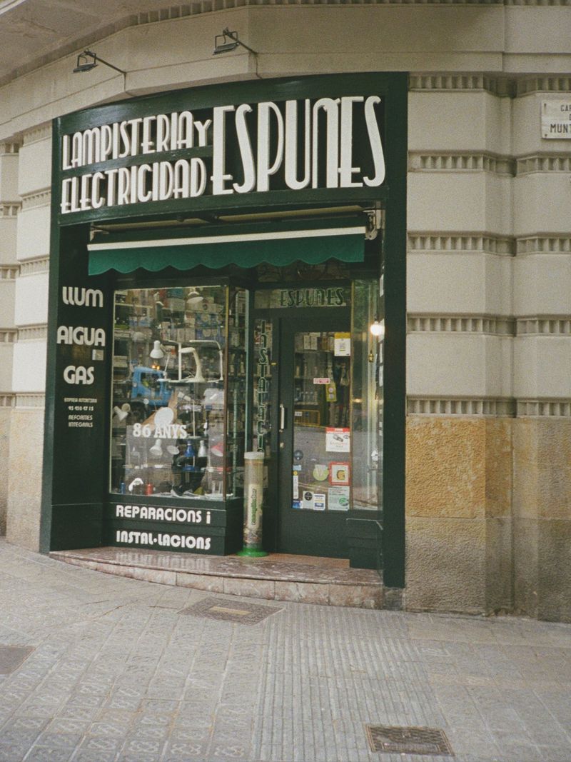 Storefront exterior of Lampisteria y Electricitat Espunes with dark green facade and large display windows on a paved street.