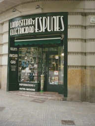 Storefront exterior of Lampisteria y Electricitat Espunes with dark green facade and large display windows on a paved street.