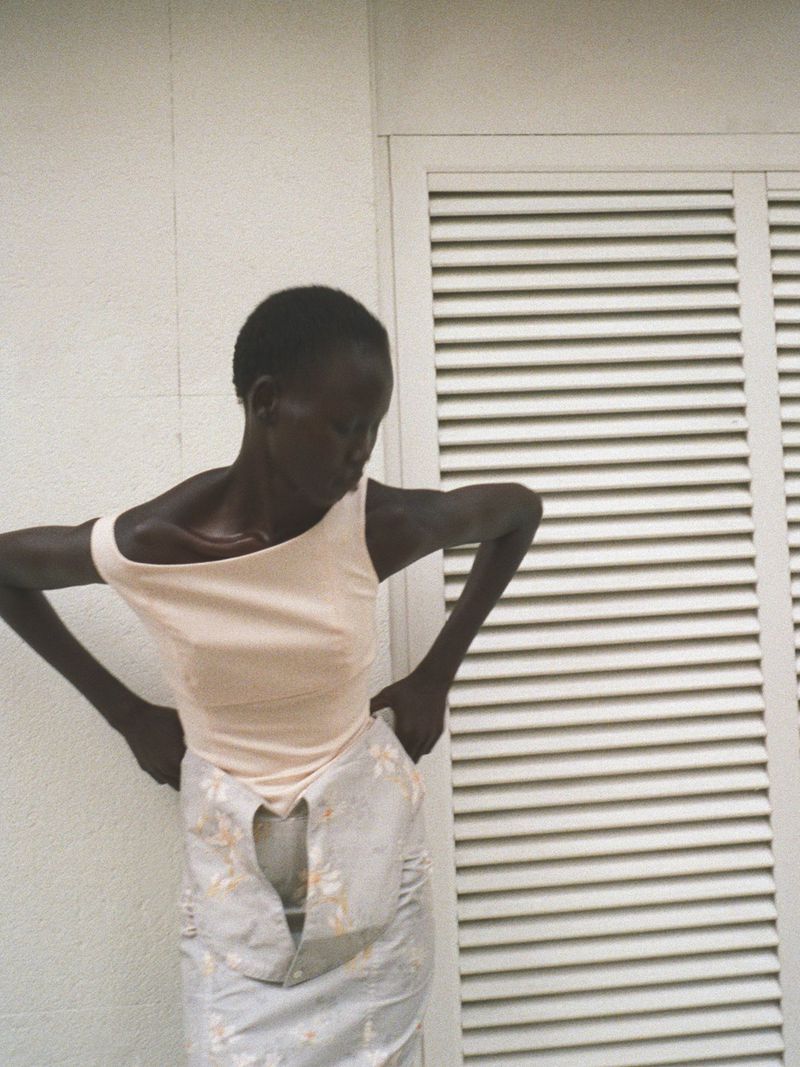 Model wearing a pale top and patterned skirt posing against a white exterior wall with louvered doors for Modern Road.