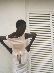 Model wearing a pale top and patterned skirt posing against a white exterior wall with louvered doors for Modern Road.