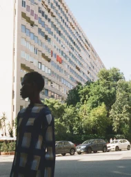 Model wearing patterned blue top standing outdoors against a large residential building for Travessera editorial