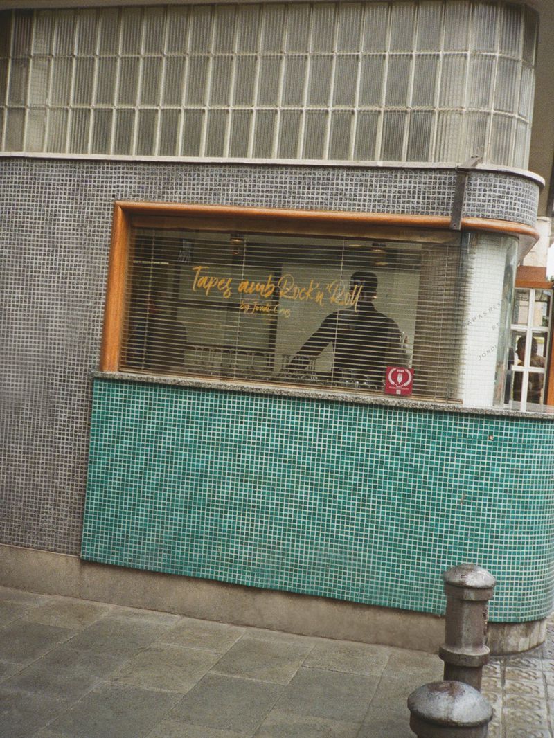 Exterior shot of a storefront with turquoise mosaic tiles, a large display window, and glass block architecture above.