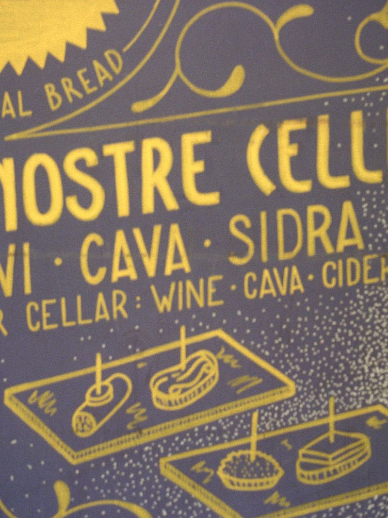 Close-up of a blue chalkboard sign with yellow handwritten chalk lettering and food illustrations for Modern Road Travessera.