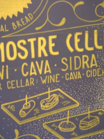Close-up of a blue chalkboard sign with yellow handwritten chalk lettering and food illustrations for Modern Road Travessera.