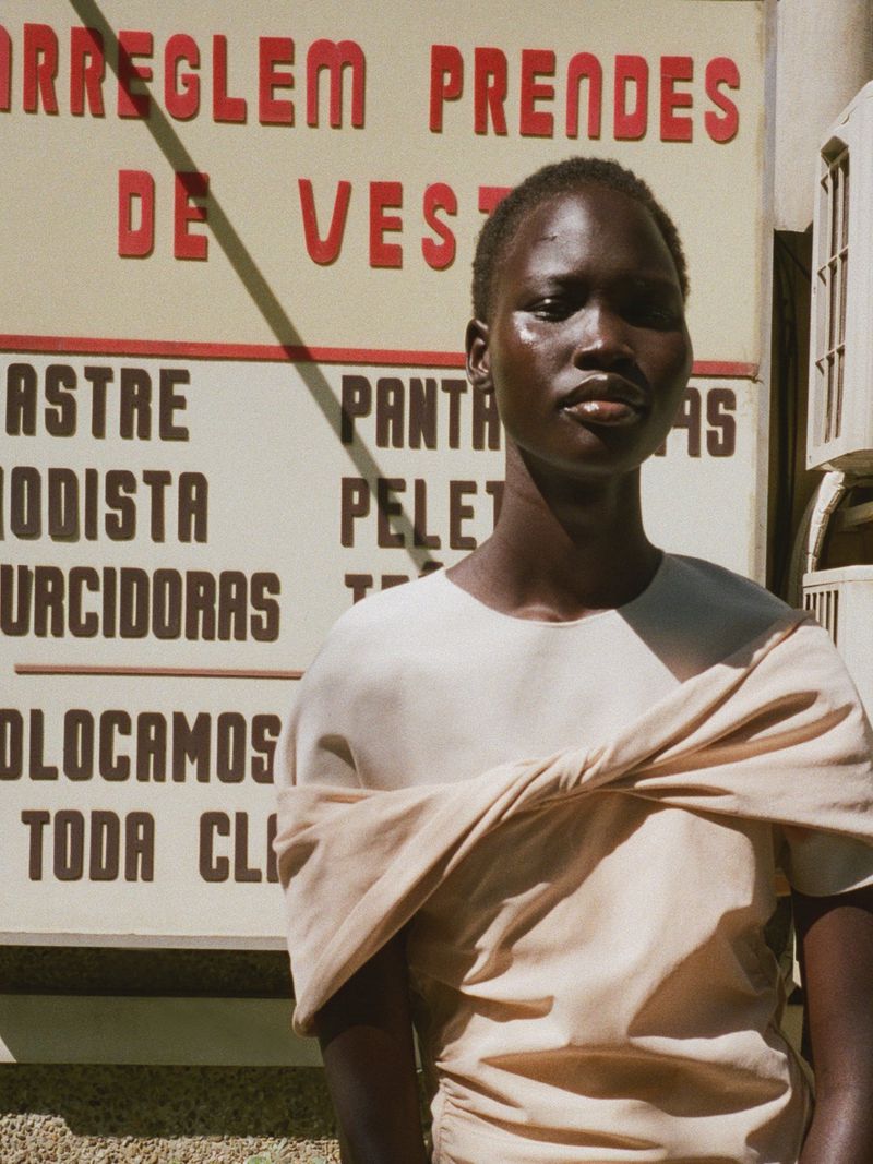 Model Chudier Billy wearing a draped cream top outdoors against a vintage sign for Travessera by Modern Road