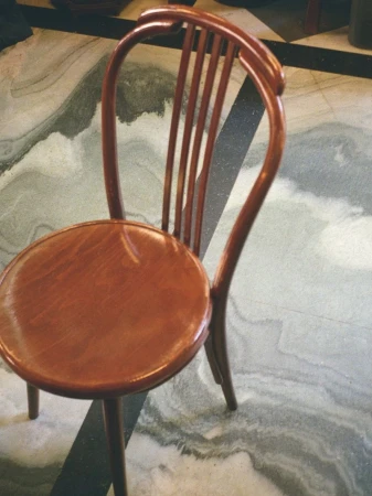 A wooden bentwood chair with a round seat and curved spindle back stands on a polished patterned marble floor.