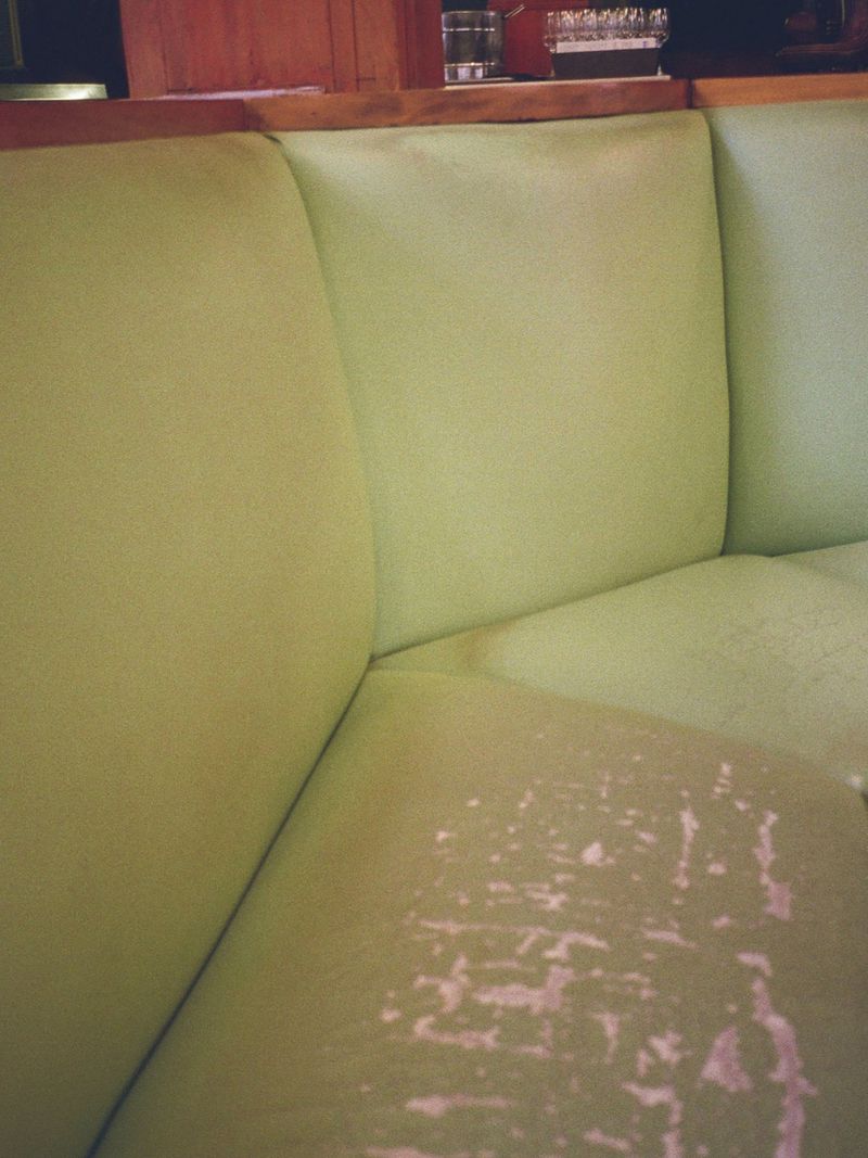 Close-up of a distressed light green upholstered booth seating in a restaurant setting.