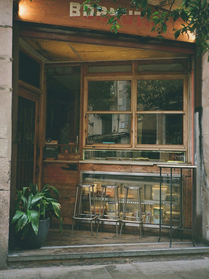 Exterior view of storefront with wooden framing, three metal bar stools, and a potted plant.