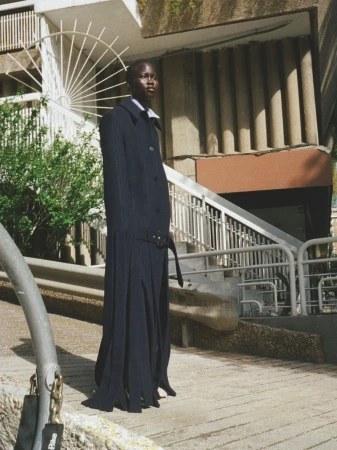 Model standing outdoors on concrete steps in a long dark navy coat with belted waist and white collar.