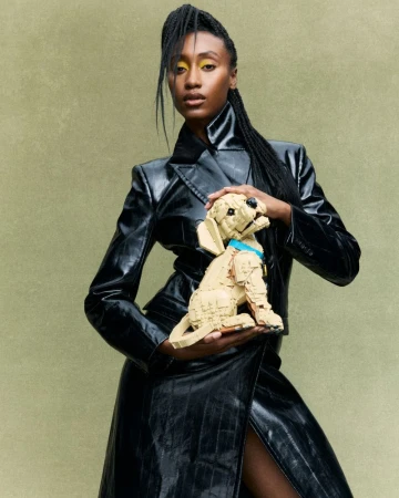 Black woman with braided hair wearing a shiny black coat holding a beige toy dog