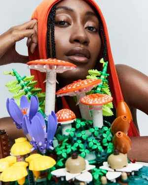 Model wearing orange hooded top behind a colorful arrangement of toy mushrooms and flowers