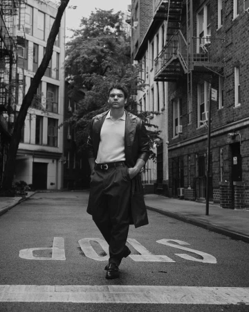 Man wearing a dark leather coat and trousers standing on a city street with a stop painted on the road