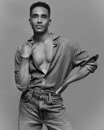 Black-and-white portrait of Jonathan Burke wearing an open denim shirt and jeans against a plain grey studio backdrop.