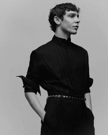 Portrait of Ben Levi Ross wearing a black collared shirt and belted trousers against a plain light grey background for V Man.