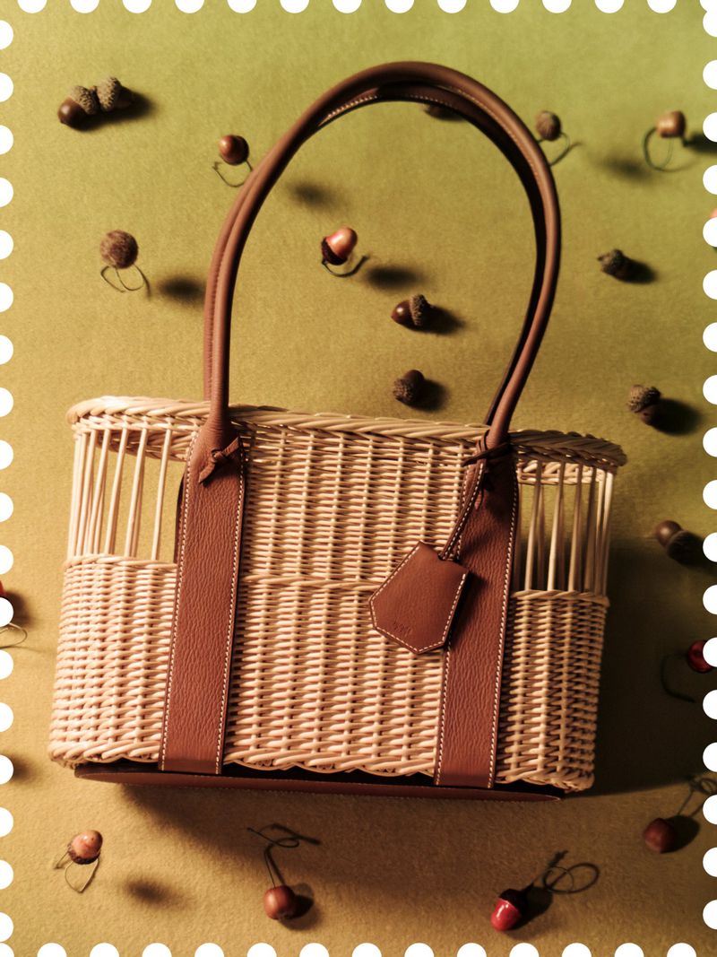 Wicker and leather handbag centered on an olive green background with scattered acorns