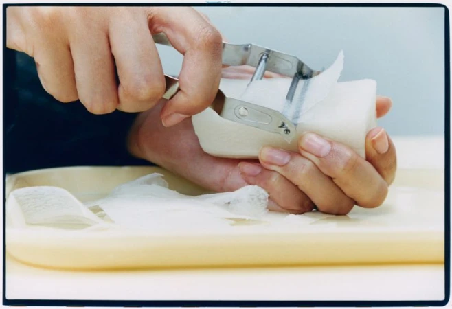 Close-up of hands using a metal peeler to peel thin layers from a white block over a tray
