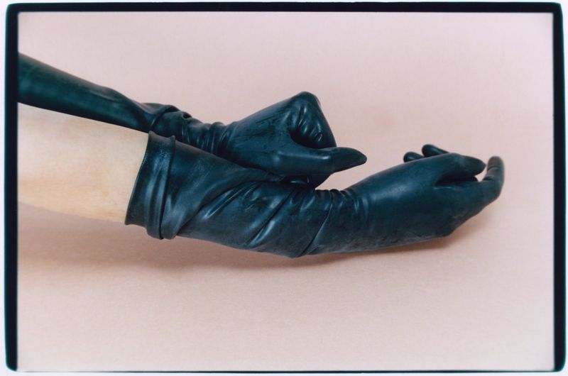 Close-up of arms wearing long black leather gloves against a plain neutral background in an editorial style photograph.