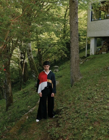 Man wearing a colour blocked top standing on a grassy path in a forest by Ivana Micic for CRUSHfanzine