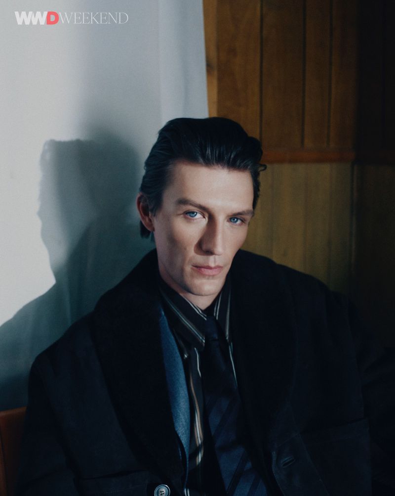 Portrait of Finnlay Davis wearing a dark coat and striped shirt against a white backdrop for WWD Neo Noir editorial