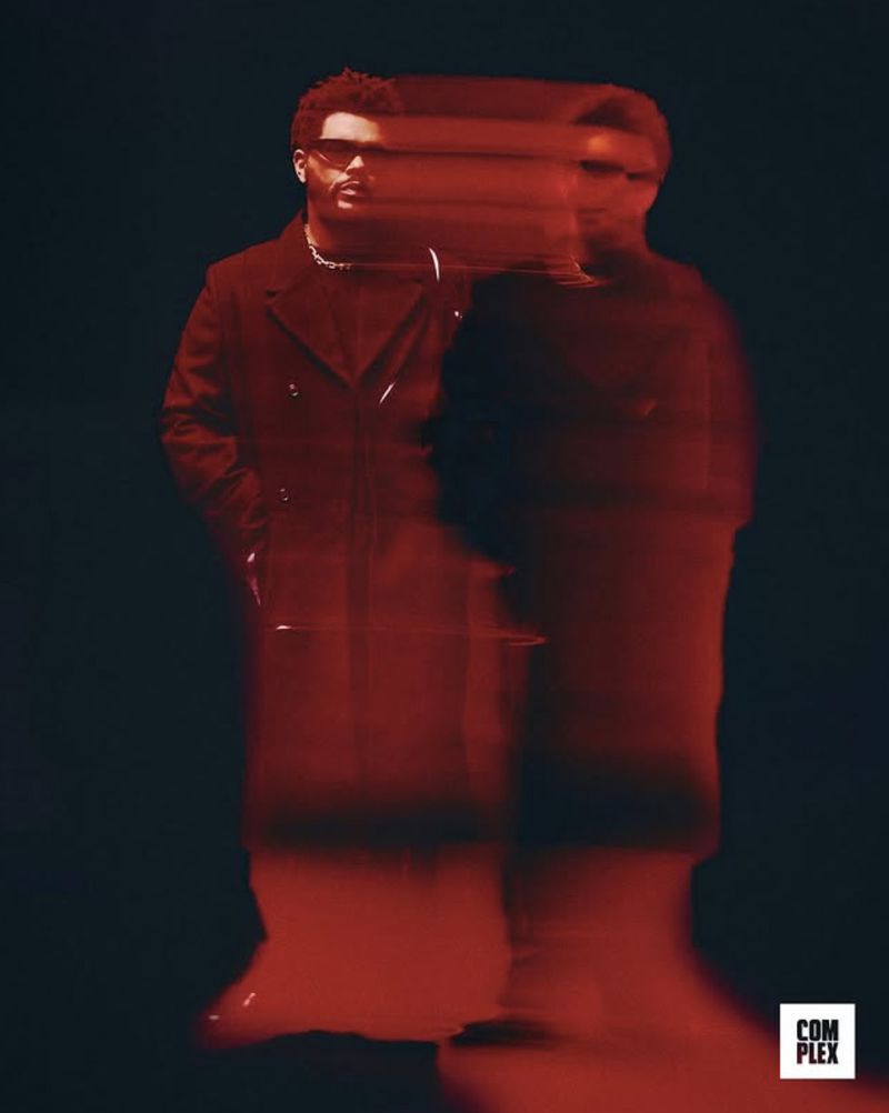 Portrait of adult male with a translucent duplication effect, wearing a dark coat and sunglasses in a dark studio setting with red lighting.