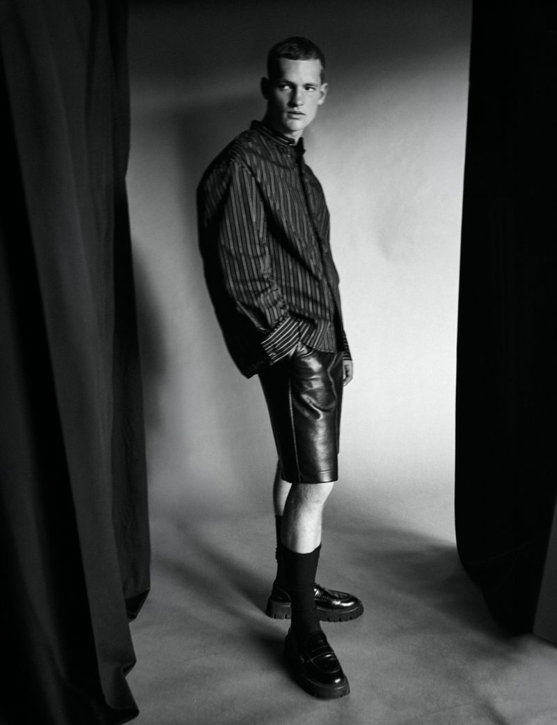 Model in striped shirt and leather shorts standing in a studio framed by dark curtains for Esquire Portugal