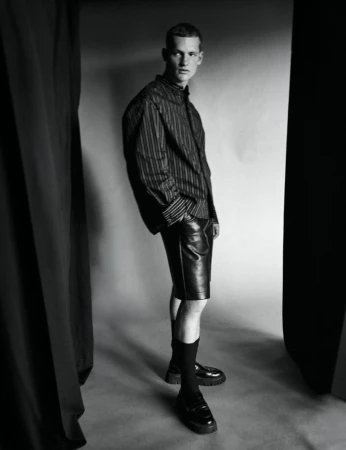 Model in striped shirt and leather shorts standing in a studio framed by dark curtains for Esquire Portugal