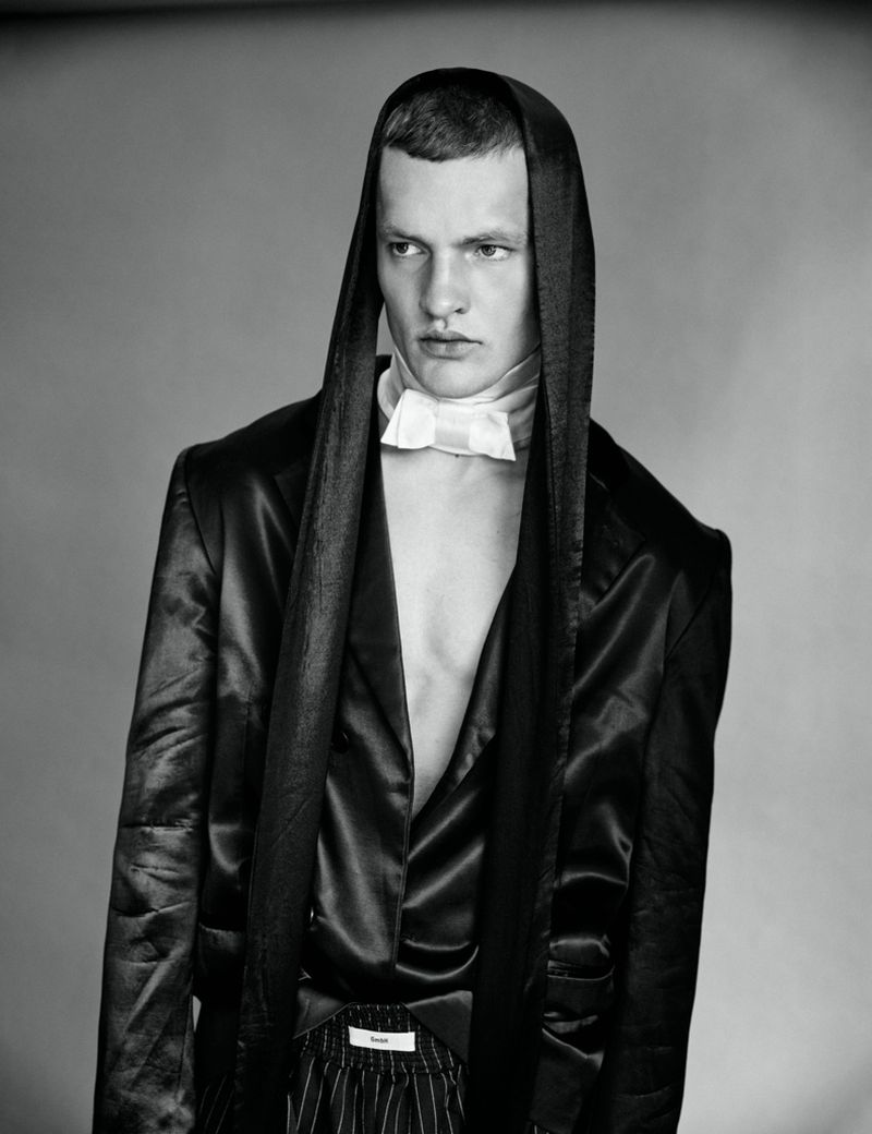Monochrome portrait of male model Ivo Pelleboer wearing a hooded satin jacket and white bowtie for Esquire Portugal.